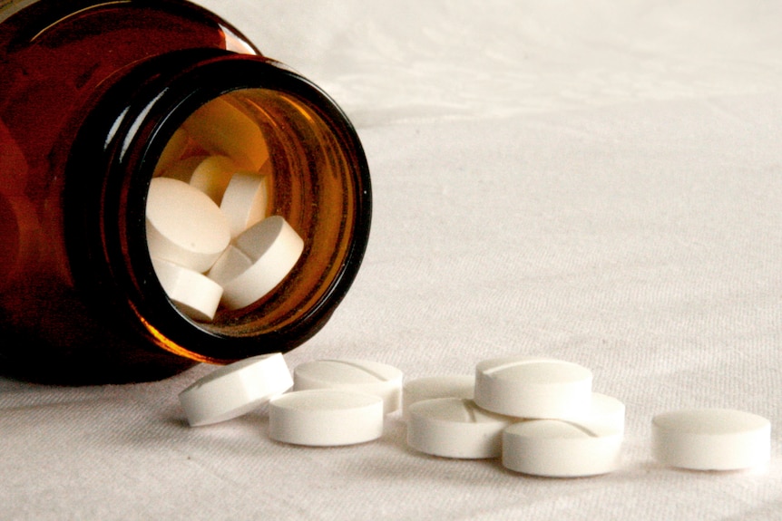 A brown medicine bottle lies on its side, spilling white tablets