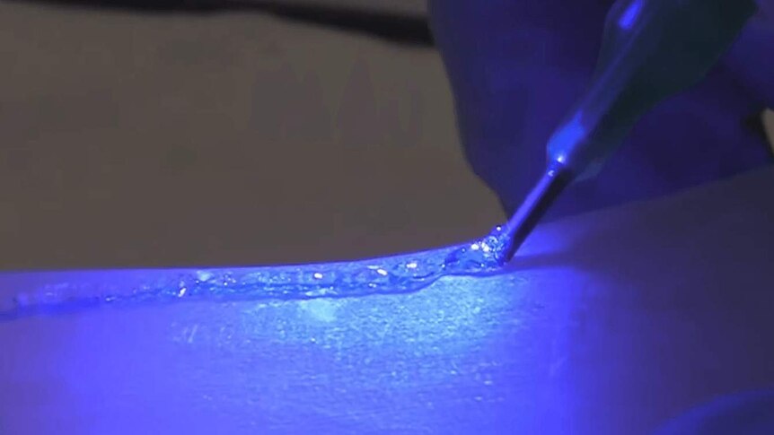 The Biopen writing a clear gel to a bone surface with a bright blue UV light shining.