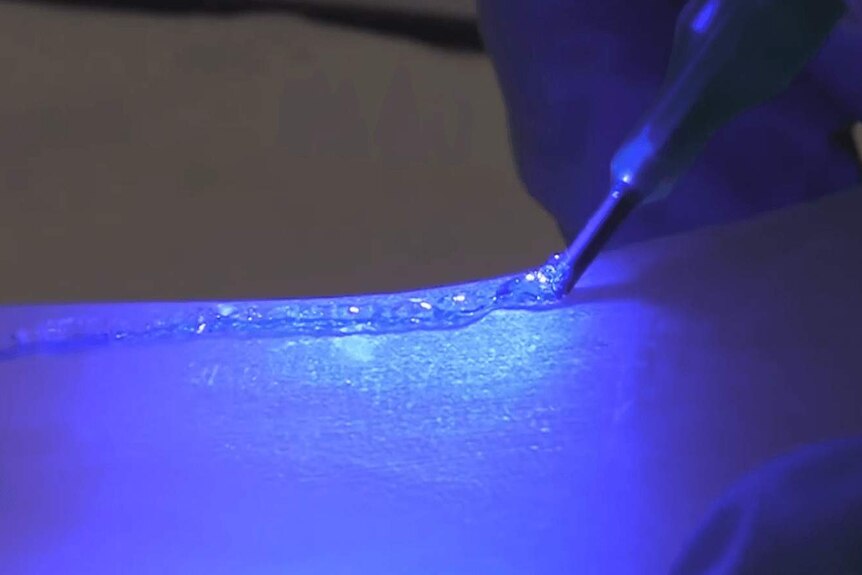 The Biopen writing a clear gel to a bone surface with a bright blue UV light shining.