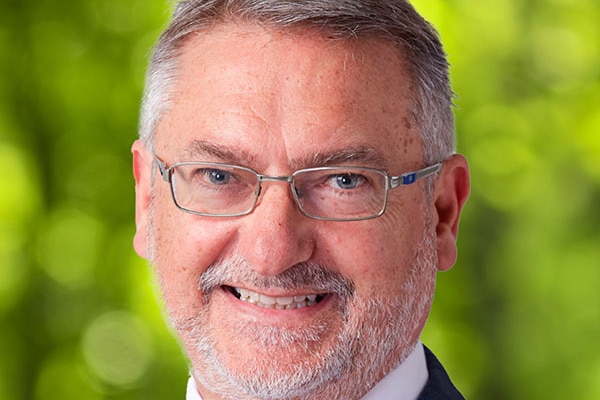 Man with glasses, grey hair wearing a red tie and blue suit smiling at camera - posed campaign photo 