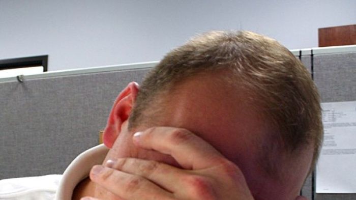 A man in an office holds his head in a distressed fashion