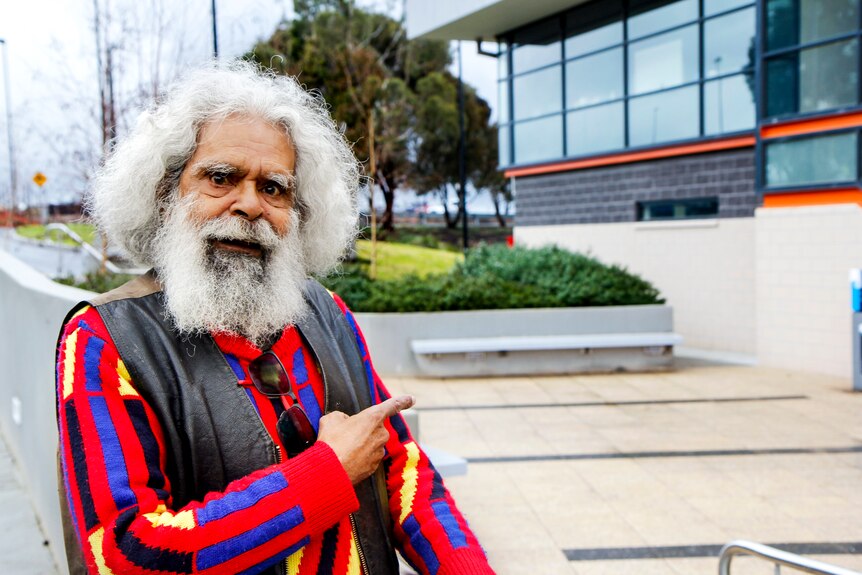 an aboriginal man with grey hair and a beard wearing a colourful jumper.