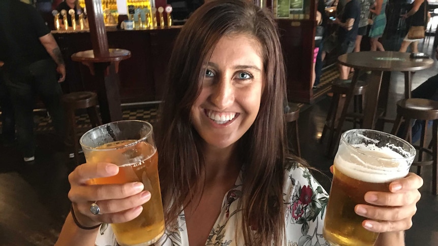 Charlotte Dubois holds two large drinks and smiles at the camera.