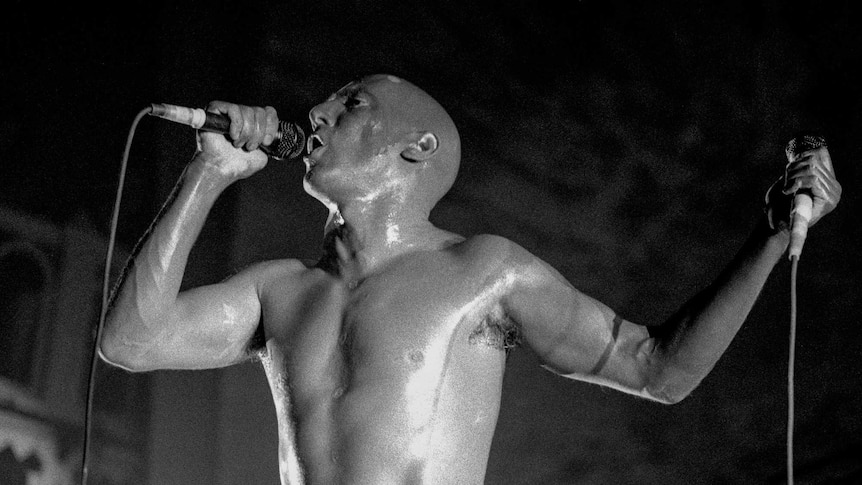 Maynard James Keenan of TOOL performing shirtless on stage in Amsterdam in February 1997. He holds two microphones.