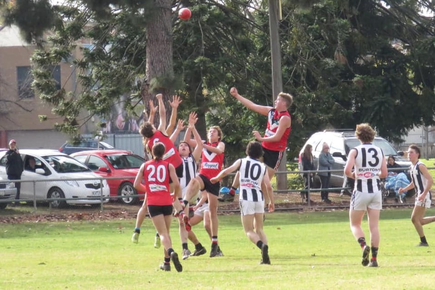 A group of players in red and black guernseys compete with players in black and white guernseys to mark the football.