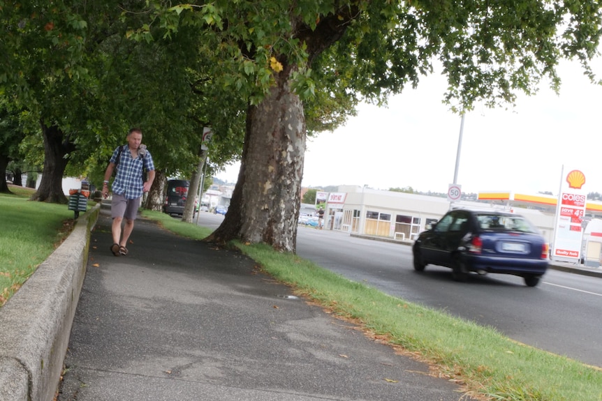 A man wearing a backpack walks along a footpath