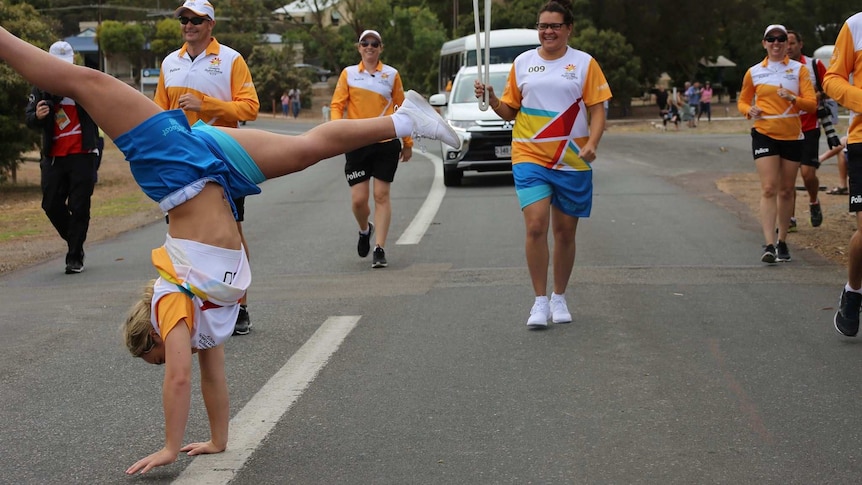 A young woman does a cartwheel in front of the Queen's Baton Relay in Coffin Bay or Port Lincoln, South Australia