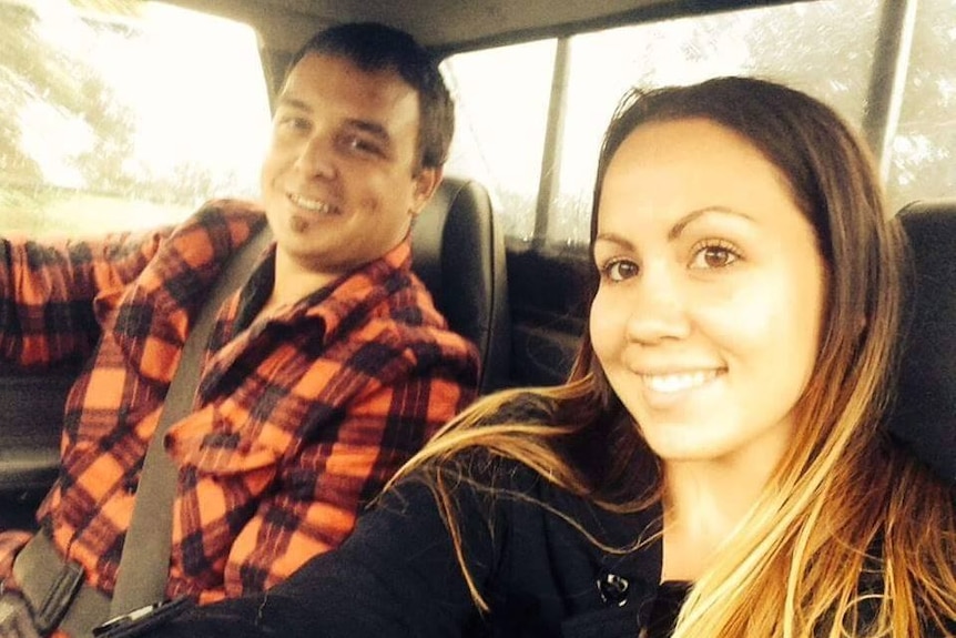 A man and a woman sit in a car smiling at the camera