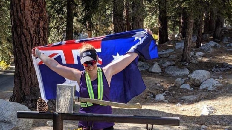 Ultra-triathlete Melissa Urie stands in front of the Mount Whitney trail with an Australian flag