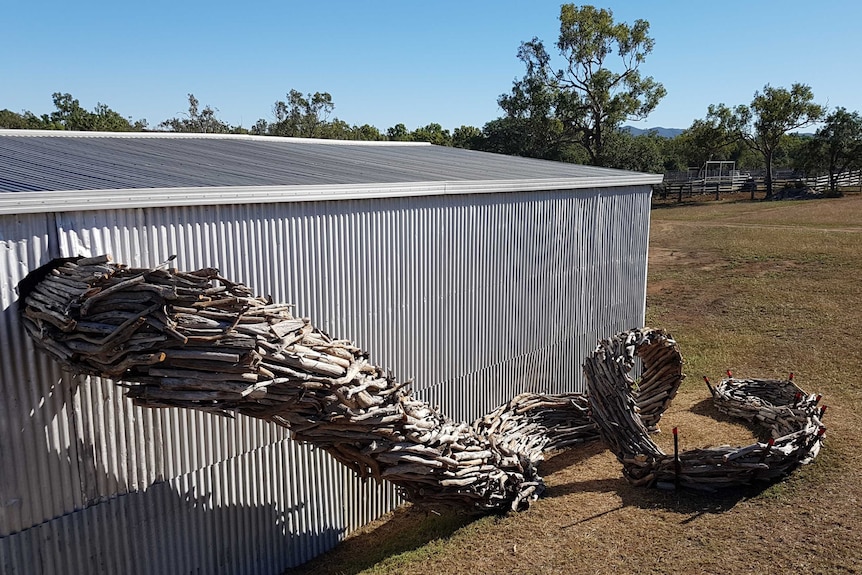 Looking over a sculpture made of timber sprouting from a shed into the ground.