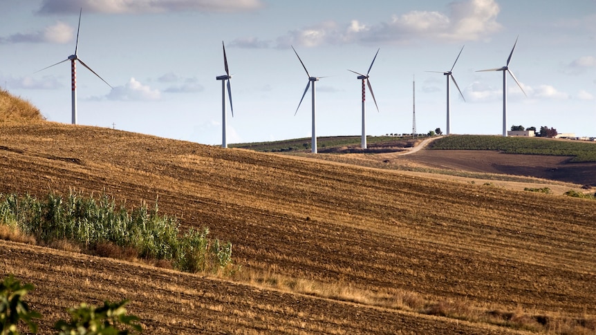 Wind turbines on a hill surrounded by fields.