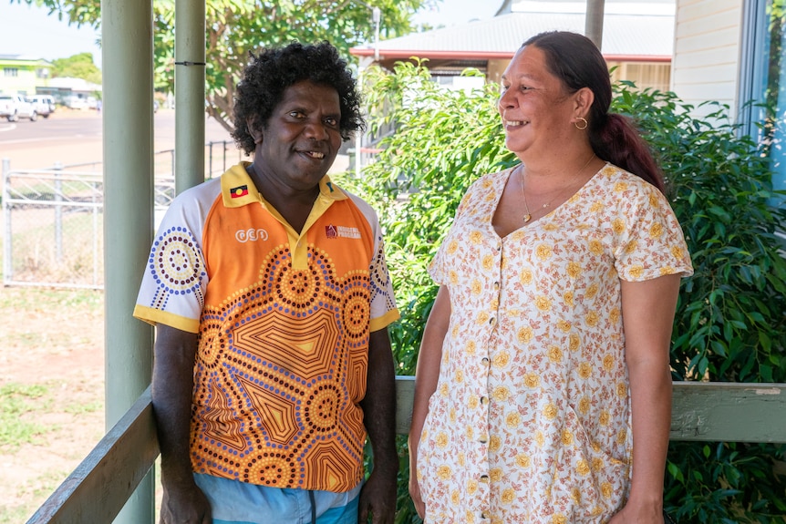 An Indigenous man and woman stand on a patio, smiling at each other.