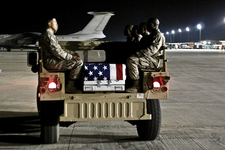 US soldiers sit in an army jeep alongside a coffin draped in the American flag