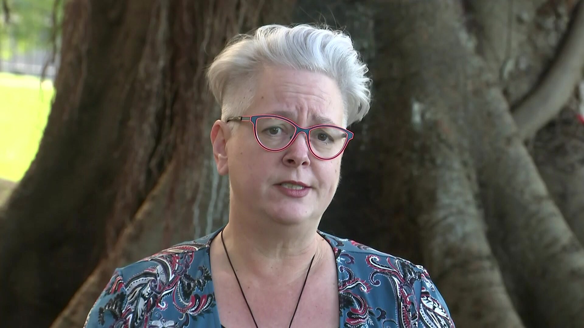 a woman wearing glasses standing outdoors speaking