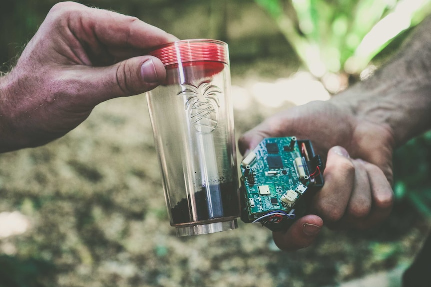 A prototype device being held against a soil sample in a jar.