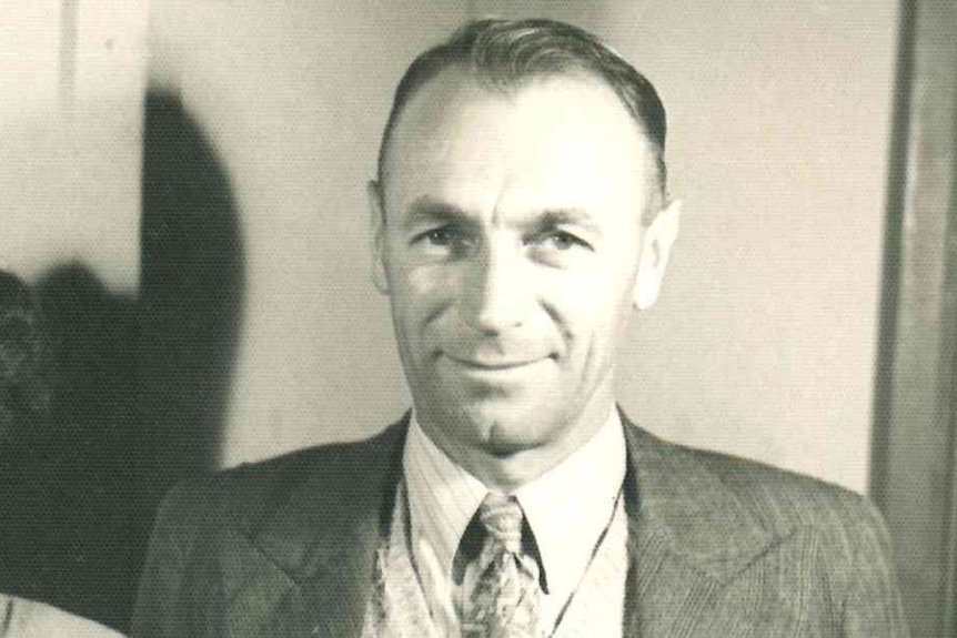 A black and white image of a man in a suit and tie smiling.