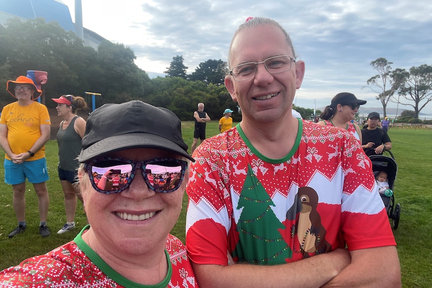 Two people in a Christmas party smile with the people around them on camera in the park