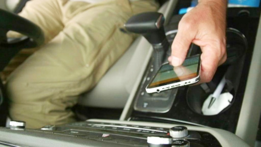 An unidentified person uses a mobile phone low near the gear changer in a car.