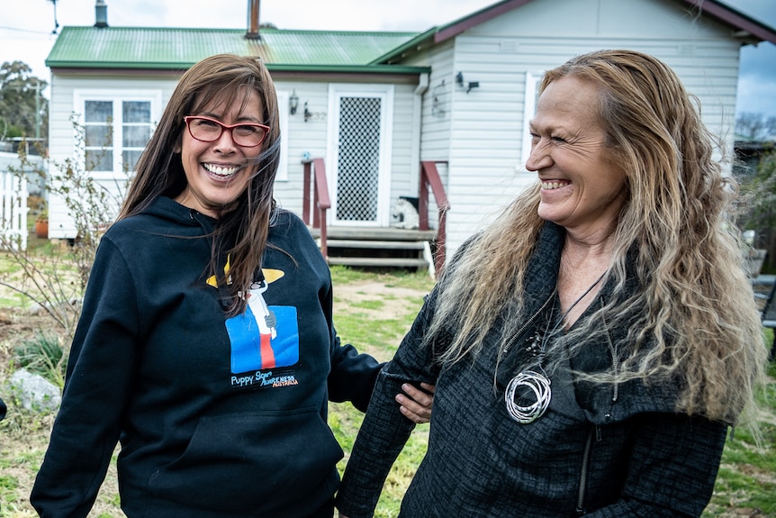 Two women laugh outside a house.