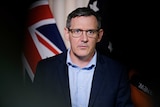 Chief Minister Michael Gunner is standing in front of a microphone with a serious expression. Behind him is the Australian flag.