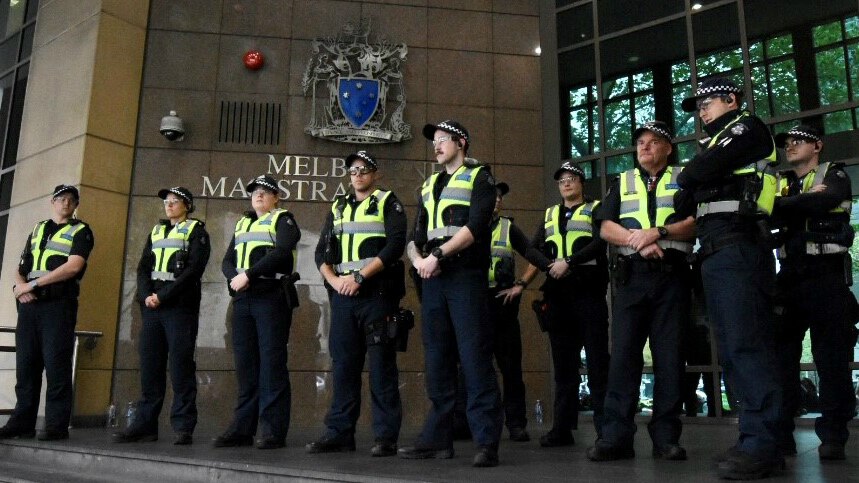 Ten police officers in uniform and yellow vests stand outside Melbourne Magistrates' Court.