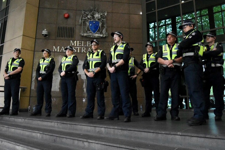 Ten police officers in uniform and yellow vests stand outside Melbourne Magistrates' Court.