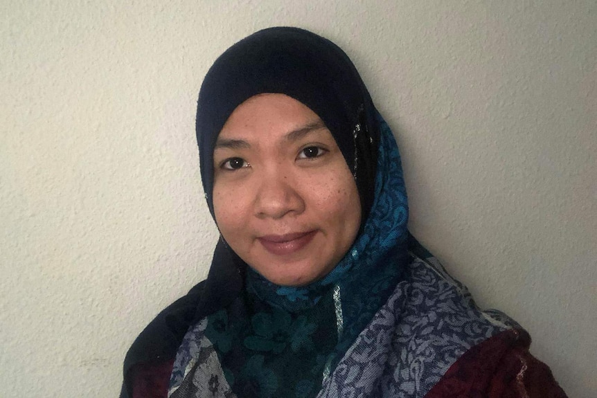 Singaporean woman Kim Assakin wearing hijab, standing in front of white wall