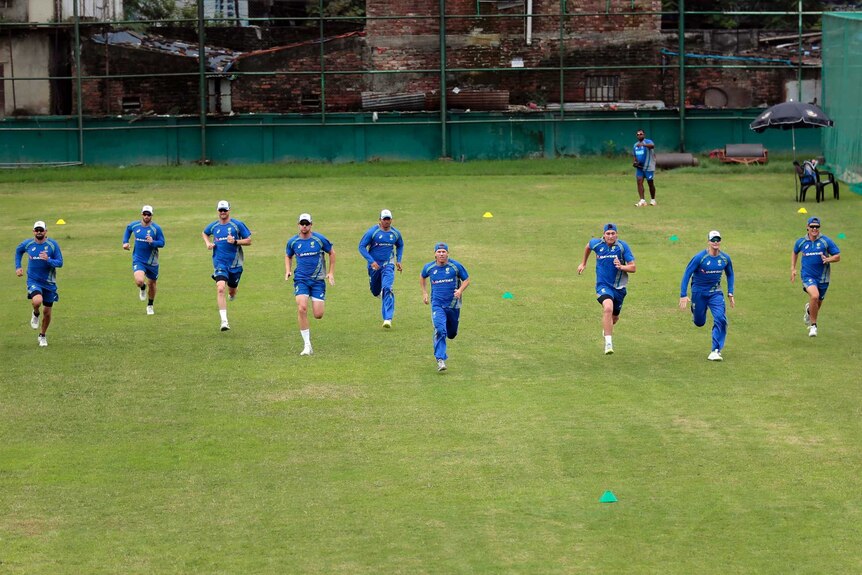 A wide shot of Australian cricket players running in a line at training.