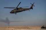 A military helicopter taking off in a desert location.