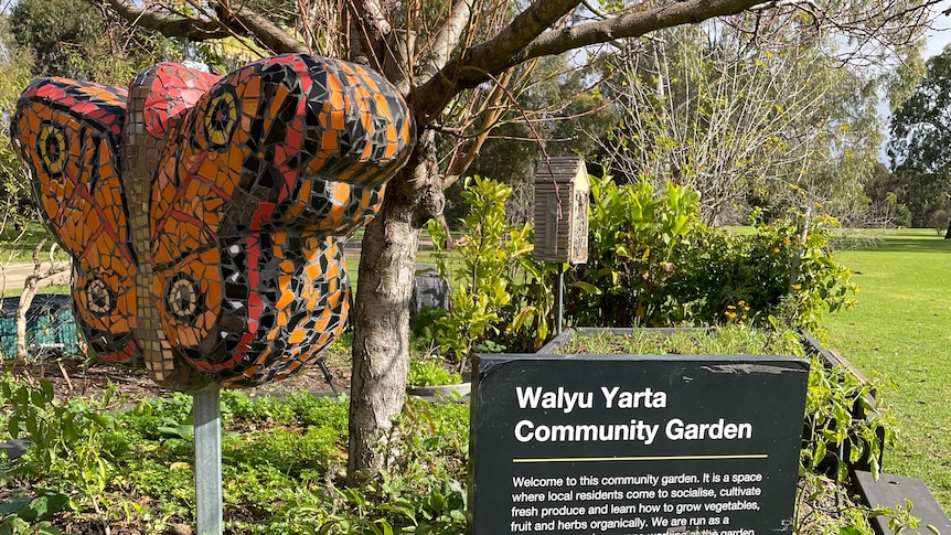 A sign for a community garden with a mosaic butterfly in it