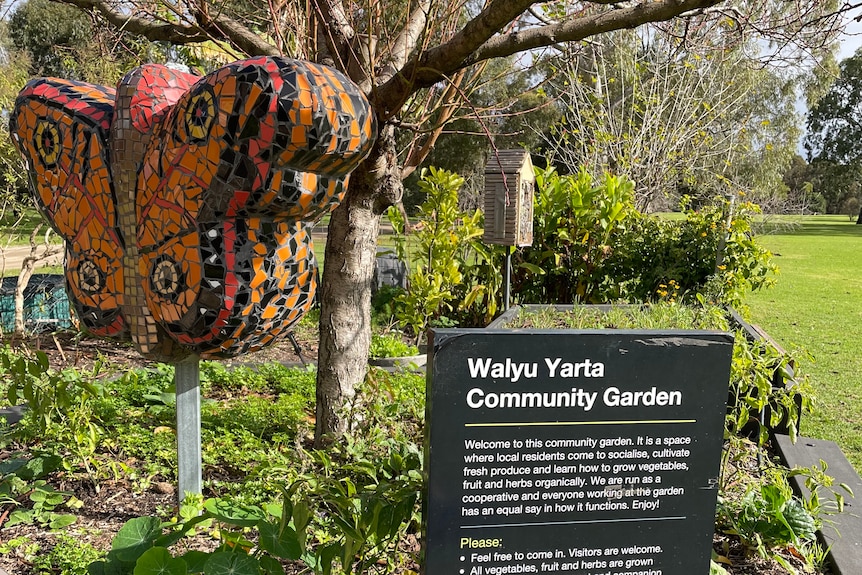 A sign for a community garden with a mosaic butterfly in it