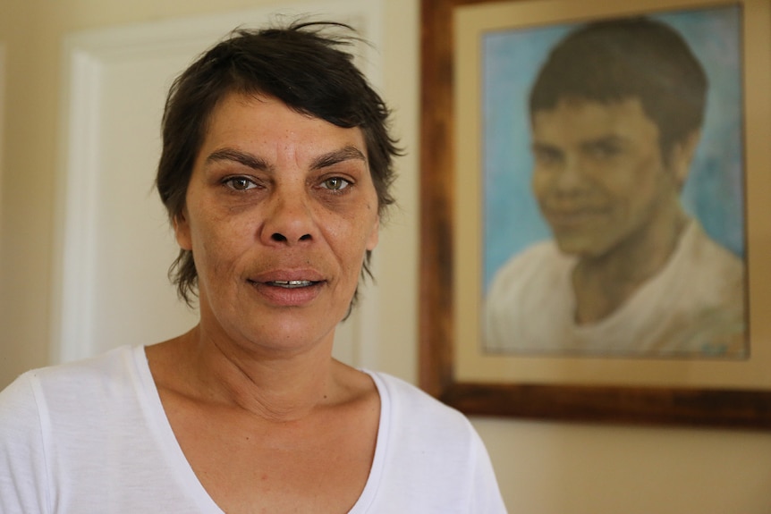 A woman pictured in front of a framed painting of her son.