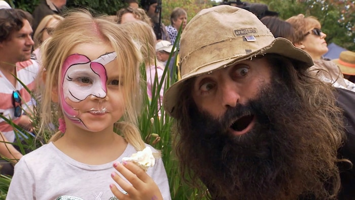 Man with beard and hat posing for camera with young girl with face paint holding an icecream