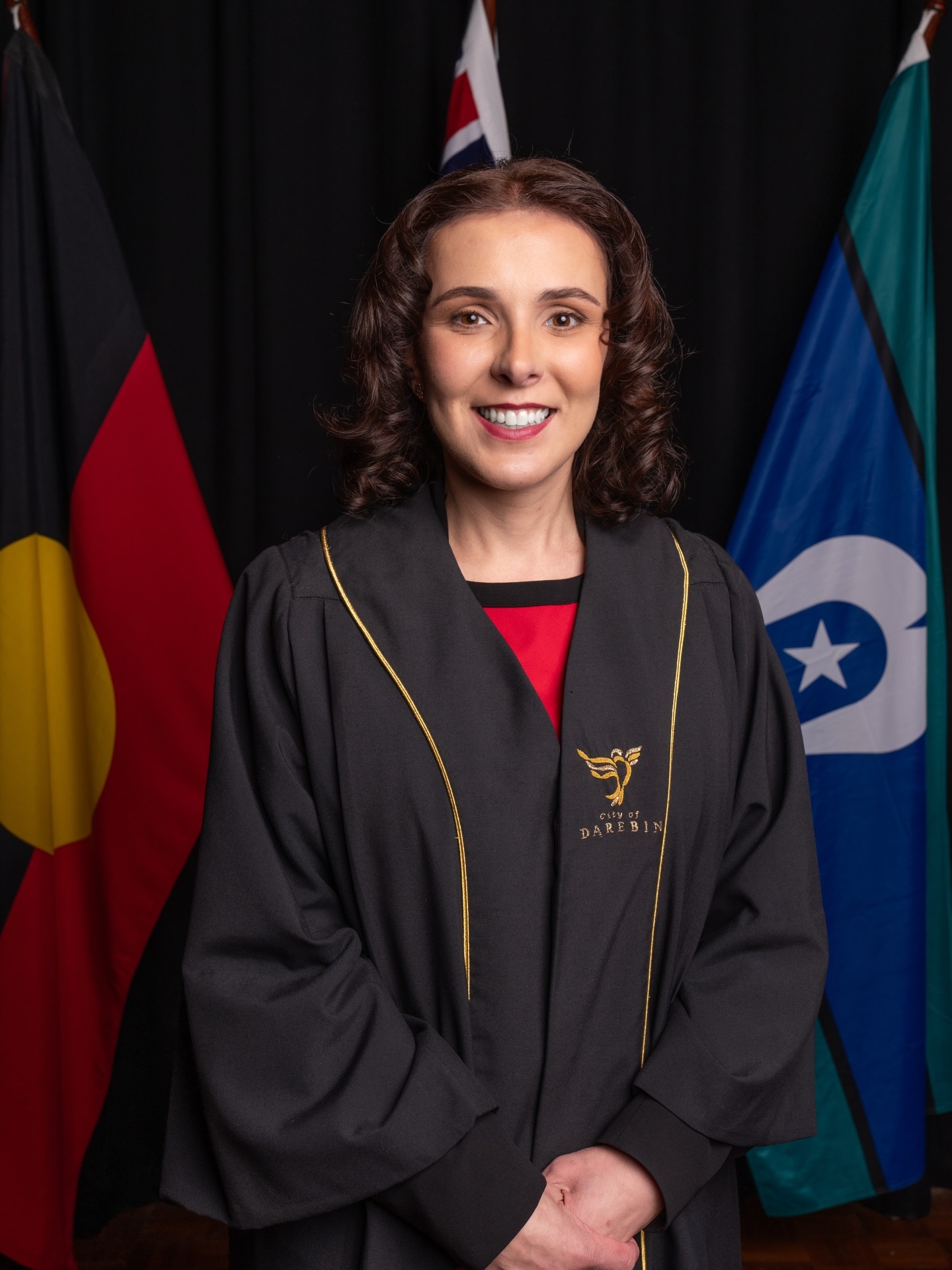 A lady with short curly brown hair smiling, flags in background