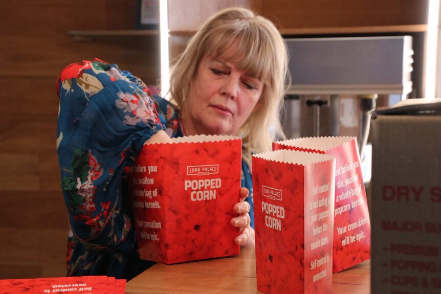 A woman reaches in a red cinema cardboard popcorn box to open it up ready for packing.