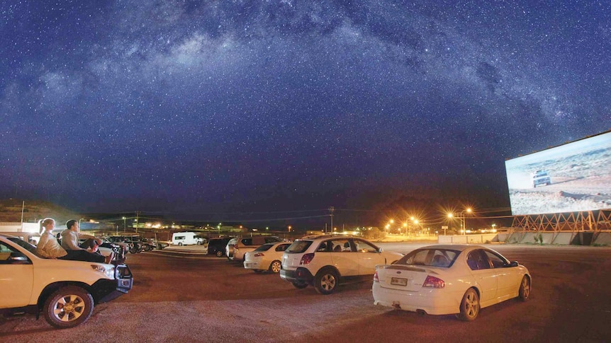 Stars shine brightly above cars parked watching a large screen.