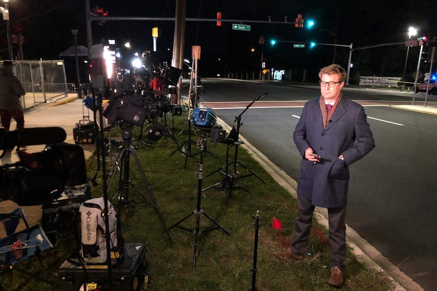 Night picture of Lipson standing on edge of road alongside lights, cameras and microphone stands.