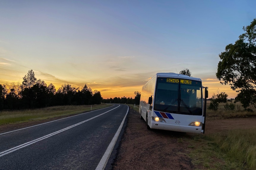 a school bus pulls off a highway onto a dirt road as dawn breaks