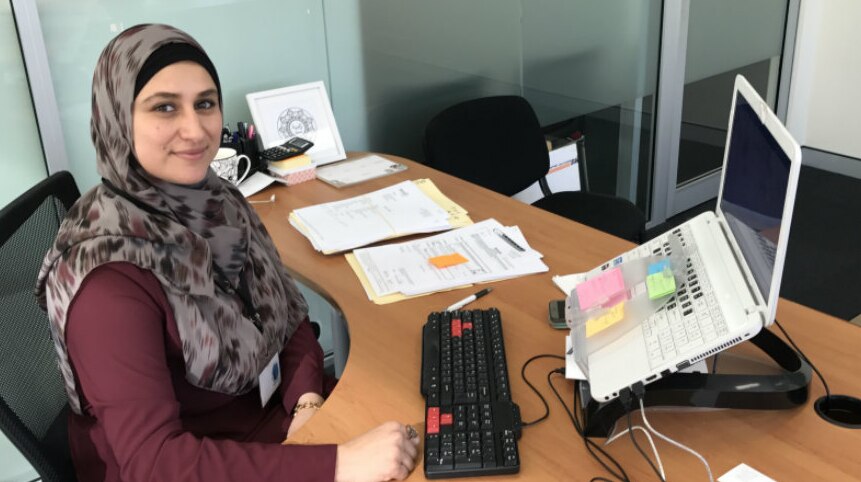 A smiling woman wearing a hijab sits at a tidy desk