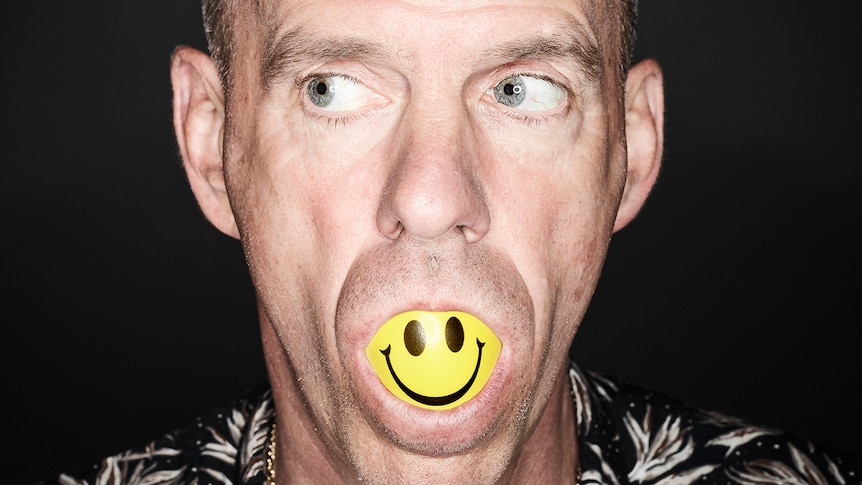 Close up of Fatboy Slim with a yellow smiley ball stuffed in his mouth