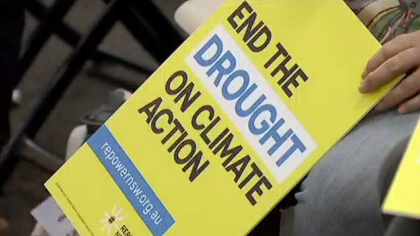 A man holds a yellow sign saying 'end the drought on climate action'
