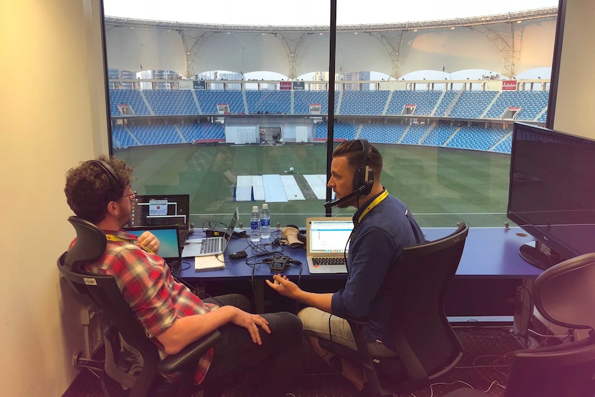 Wide shot of two men sitting in a commentary box.