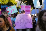 A woman in a crowd holds a pink sign that says "protect reproductive rights" in front of her face.