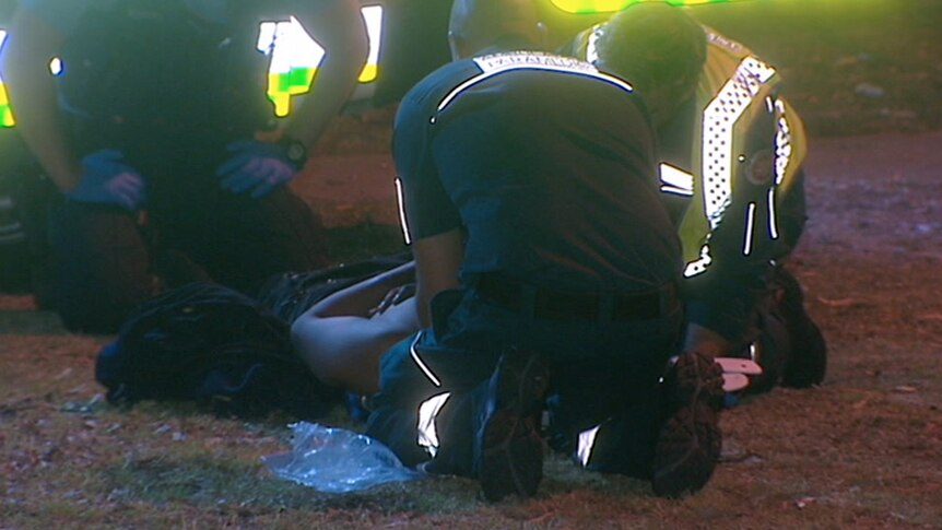 Three paramedics kneel on the ground outside treating a man lying on the ground.