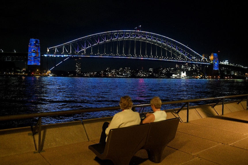 Two people sit looking at Sydney Harbour Bridge