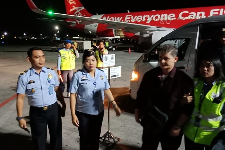 Renae Lawrence is flanked by Indonesian security officials. A plane sits in the background.