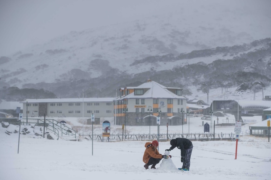 Two people make a snow man in the middle of a ski field.