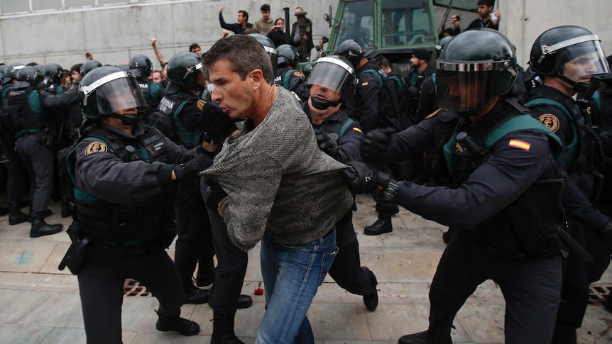 Three police in riot gear wrestle with a man.