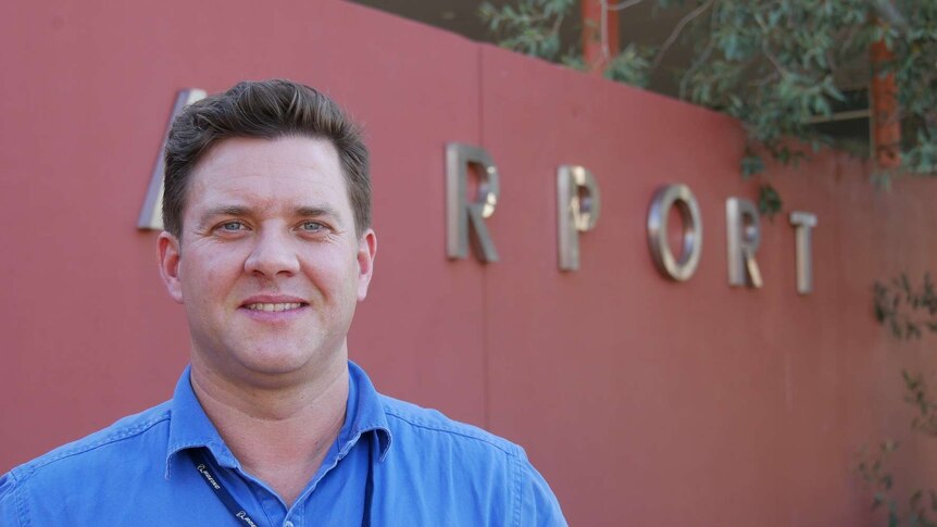 Tom Vincent in front of the Alice Springs Airport sign smiles at the camera.