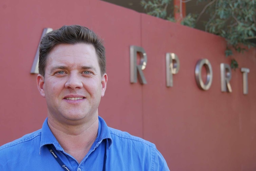 Tom Vincent in front of the Alice Springs Airport sign smiles at the camera.